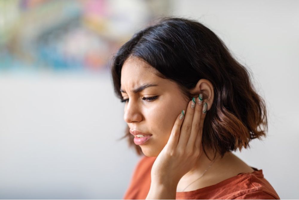 Woman holding jaw in discomfort, illustrating TMJ pain or ear-related jaw tension