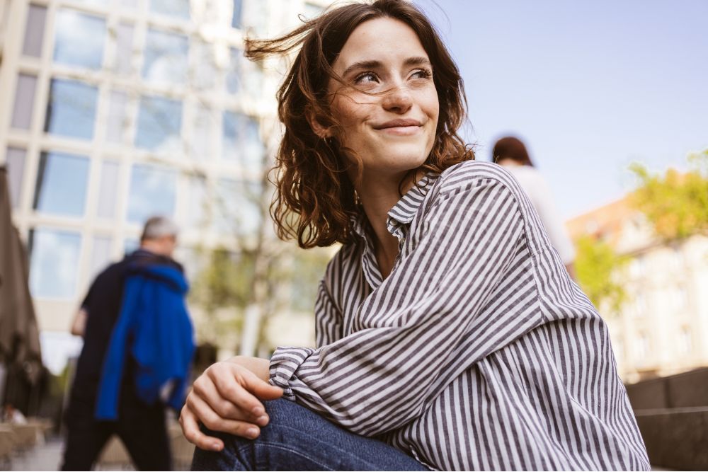 Woman sitting outdoors with a relaxed smile, representing confidence and comfort after dental care