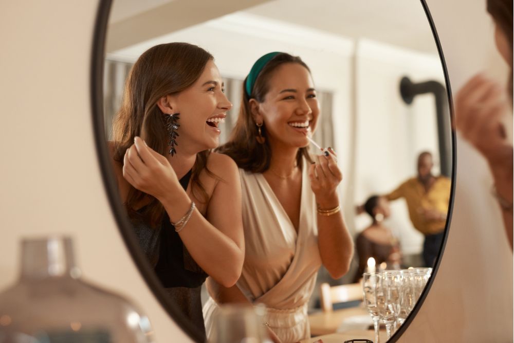 Two women smiling in a mirror while getting ready, representing confidence in a bright, healthy smile