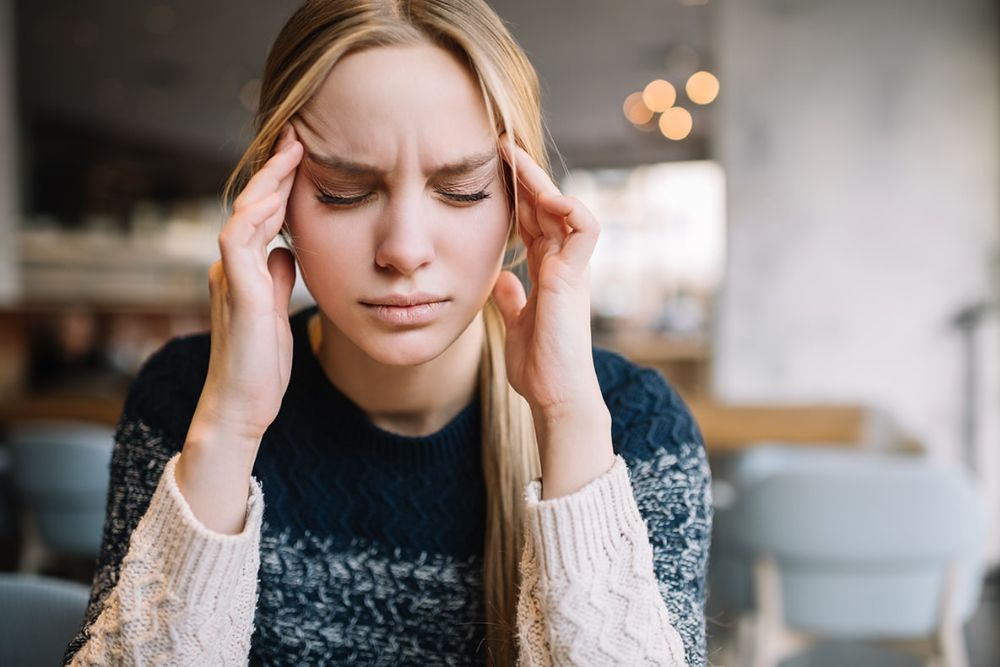 Woman holding temples in pain, illustrating headaches or TMJ-related jaw tension
