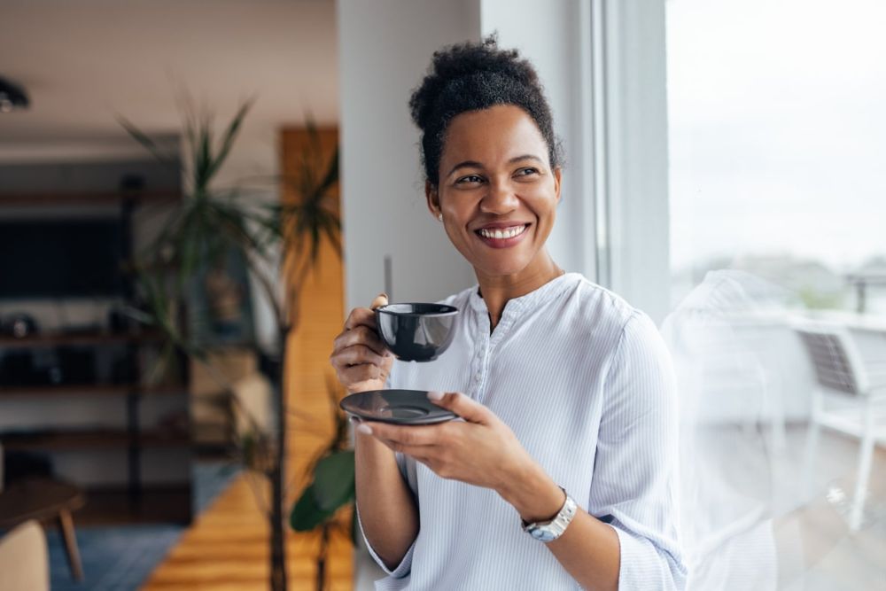 Smiling woman enjoying a hot drink comfortably, representing relief from tooth sensitivity after dental care