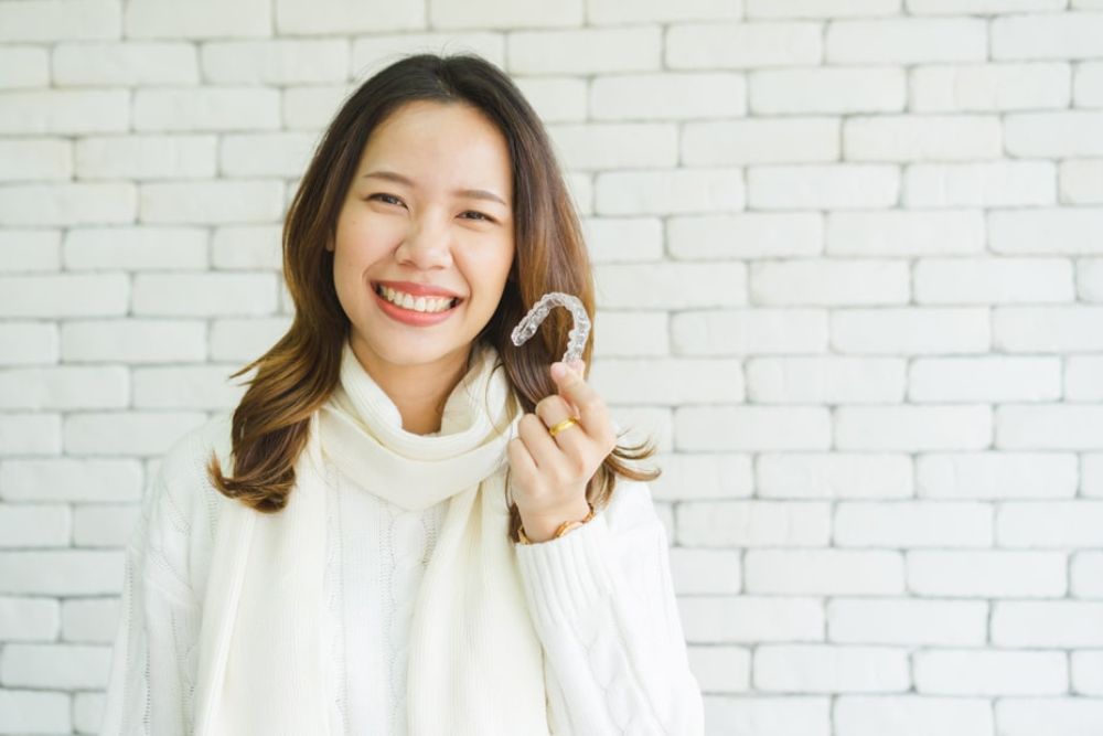 Woman holding clear aligner and smiling, representing discreet orthodontic treatment like Invisalign