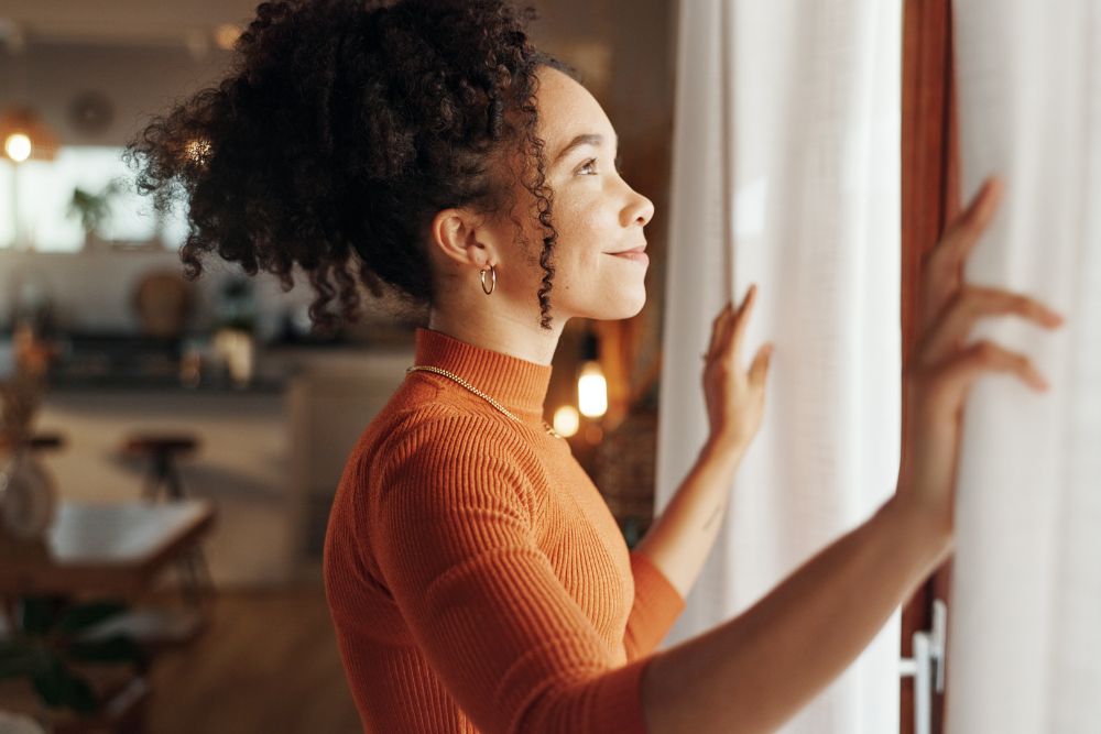 Woman looking out window with a calm smile, representing confidence and well-being after dental care