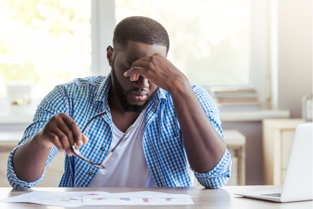 Man at desk holding glasses and pressing temples, suggesting stress, headaches, or TMJ-related pain